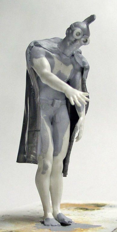 Figurine de super-héros en cape avec apprêt gris, présentant les ombrages de pré-peinture du modèle