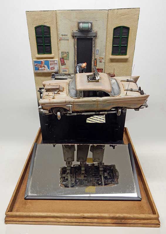 Diorama Space Chevy montrant une Chevrolet vieillie sur pattes mécaniques au-dessus d'un miroir reflétant ses jambes robotiques