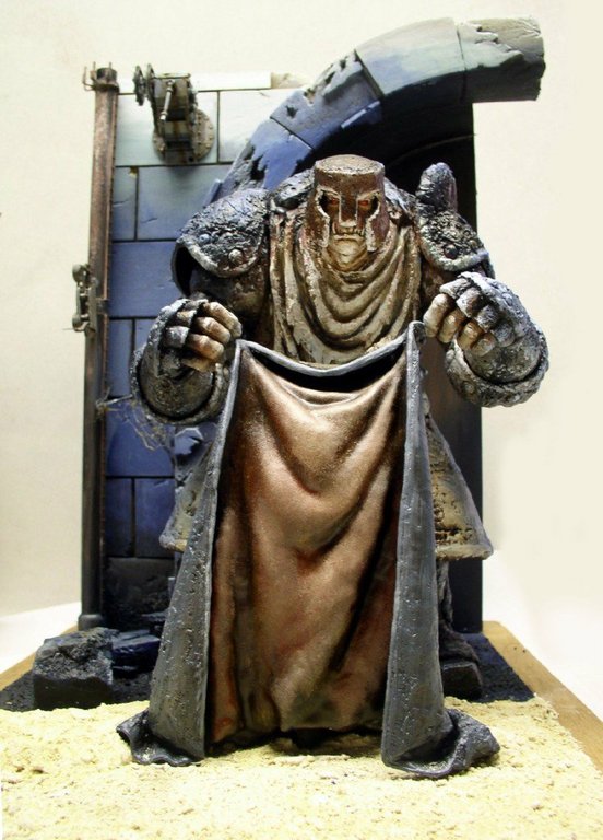 Figurine de gardien encapuchonné tenant une cape devant un mur de pierre
