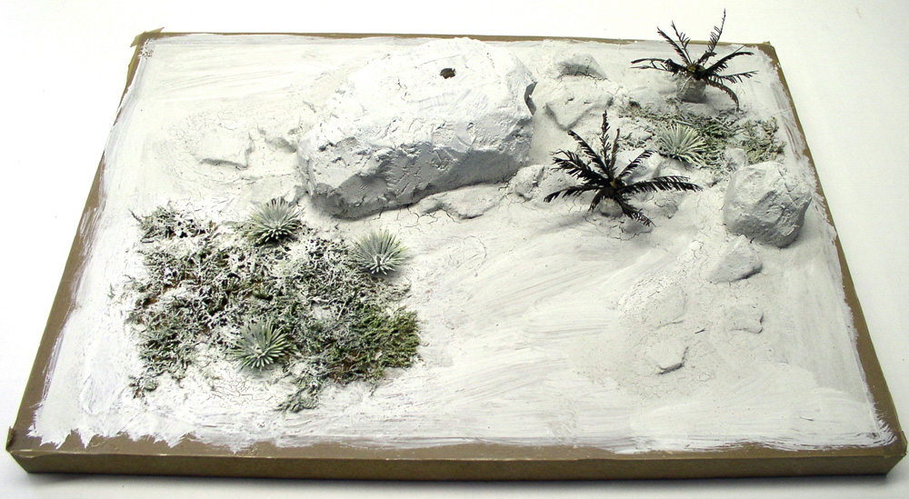 Diorama de maquette en cours avec rochers blancs, végétation et palmiers miniatures sur socle