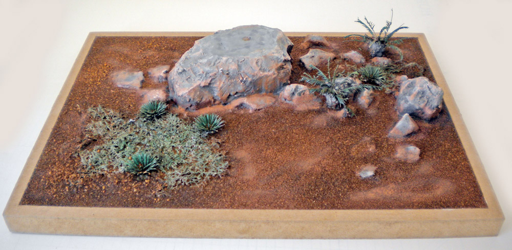 Diorama de sol désertique ocre avec gros rocher, pierres et végétation pour maquette de Velociraptor