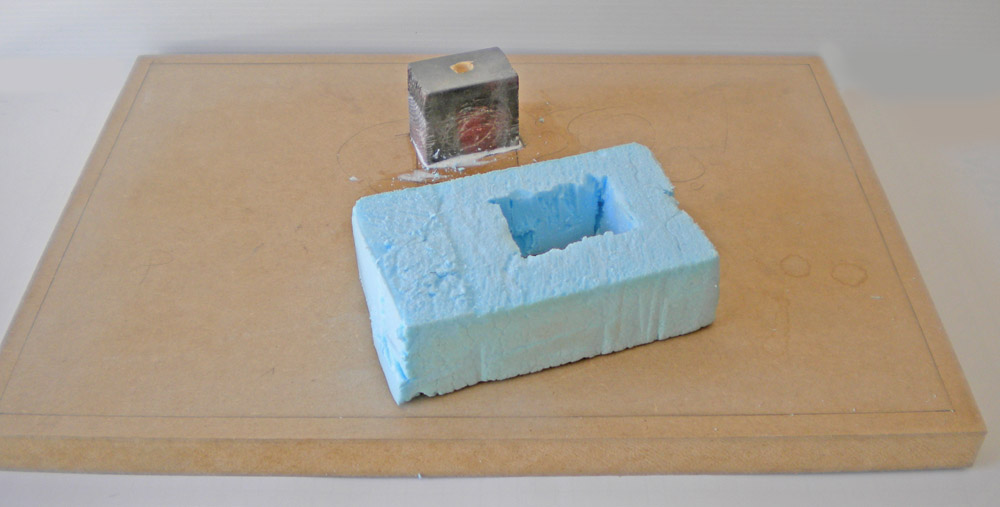 Bloc de mousse bleue évidé et socle métallique posés sur une planche de travail