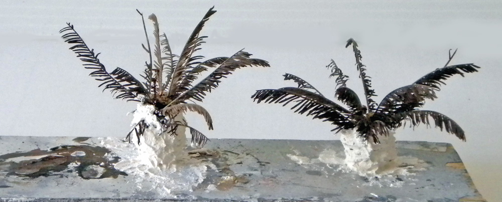 Deux maquettes de palmiers aux troncs blancs et frondes sombres sur support de travail
