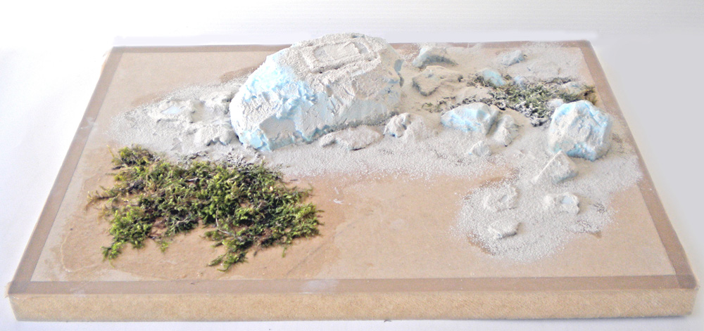 Maquette de diorama en construction avec rochers clairs, sable et végétation pour scène Velociraptor