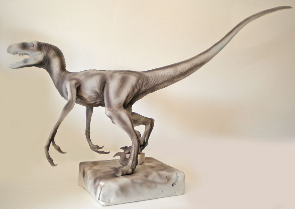 Maquette de Velociraptor gris en pleine course sur un socle rocheux clair