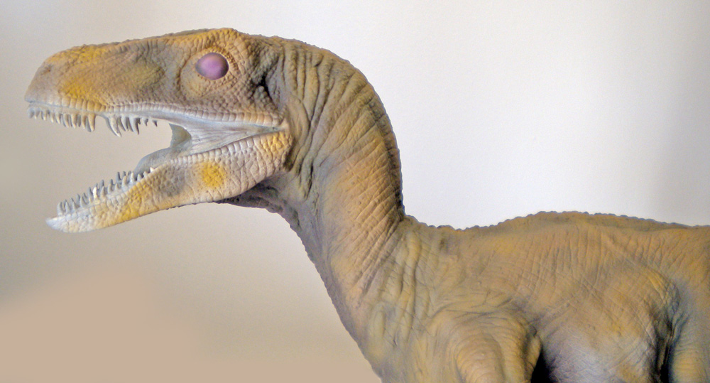 Tête de maquette de Velociraptor gueule ouverte montrant dents acérées et œil violet