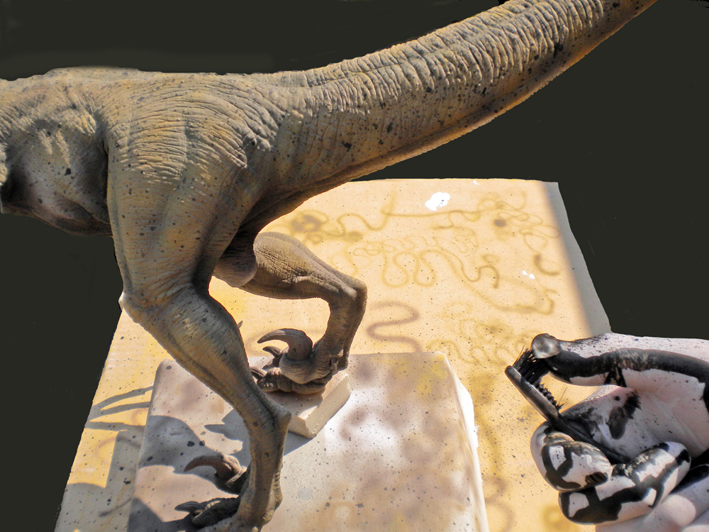Maquette de Velociraptor peinte montrant les pattes griffues posées sur un socle texturé