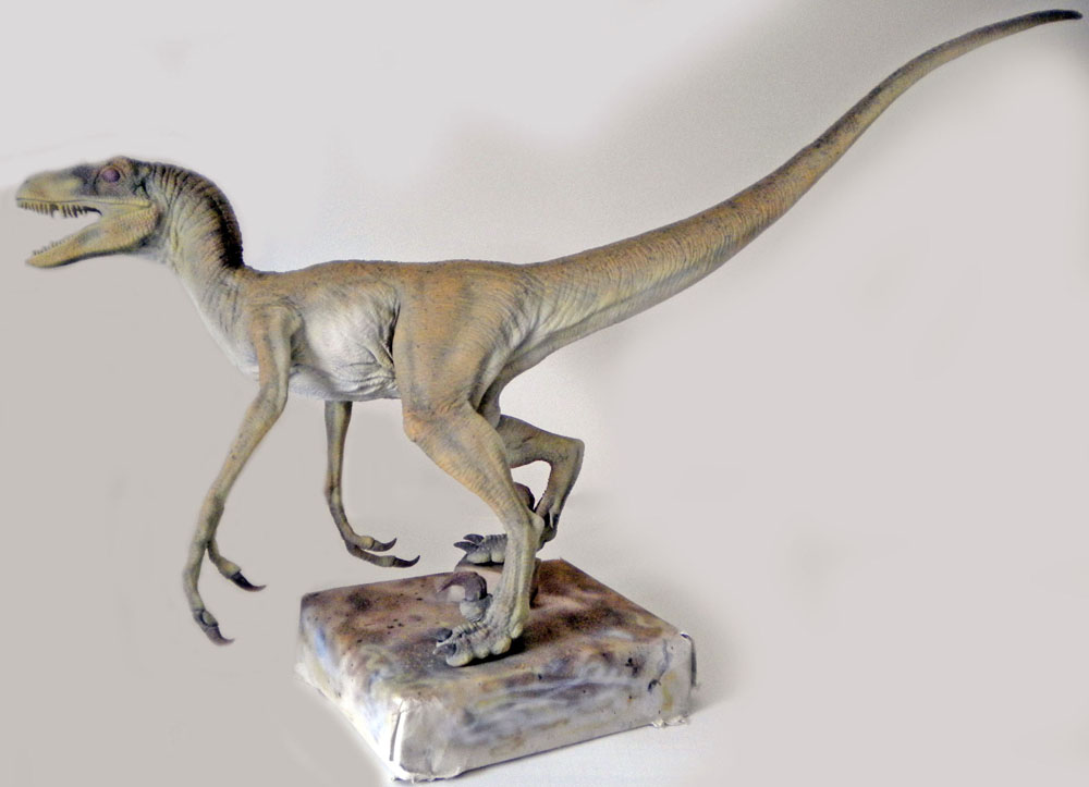 Maquette de Velociraptor peinte en teintes claires sur socle, gueule ouverte et longue queue