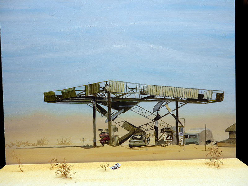 Diorama d'une station-service abandonnée dans le désert avec véhicules et toile de fond peinte