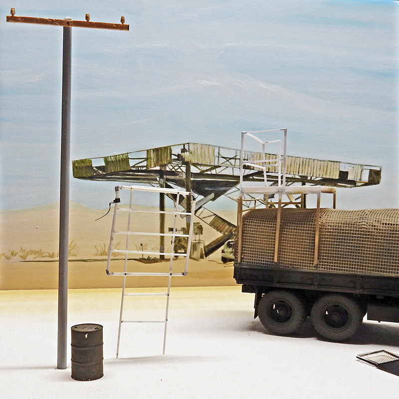 Maquette de camion militaire bâché dans un décor désertique avec poteau, échelle et baril