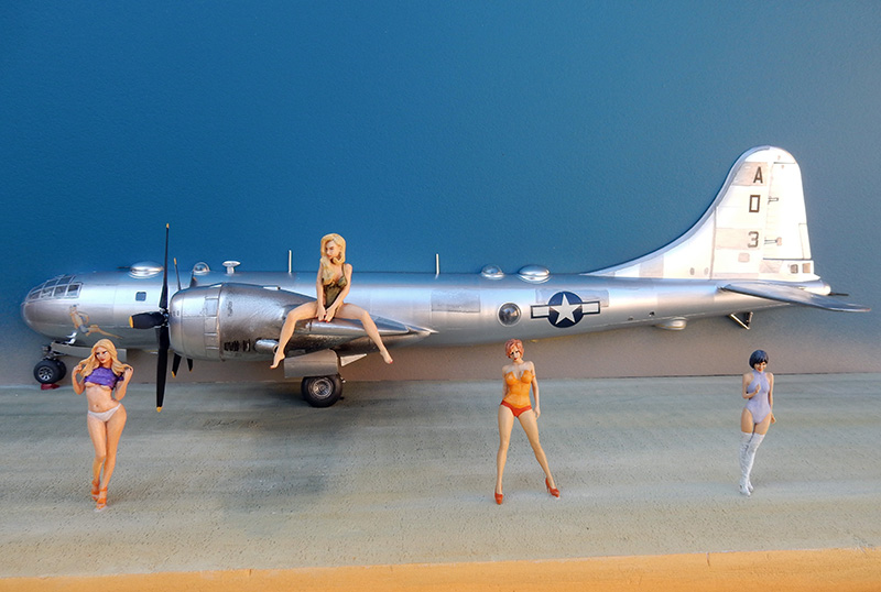 Maquette de bombardier B-29 argenté entouré de figurines pin-up sur fond bleu