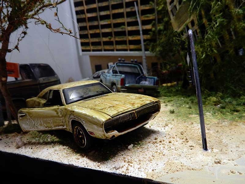 Diorama post-apocalyptique avec voiture américaine rouillée abandonnée parmi végétation envahissante et bâtiments en ruine