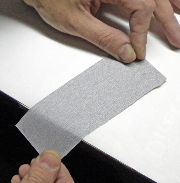Mains tenant une bande de papier de verre gris pour poncer une maquette