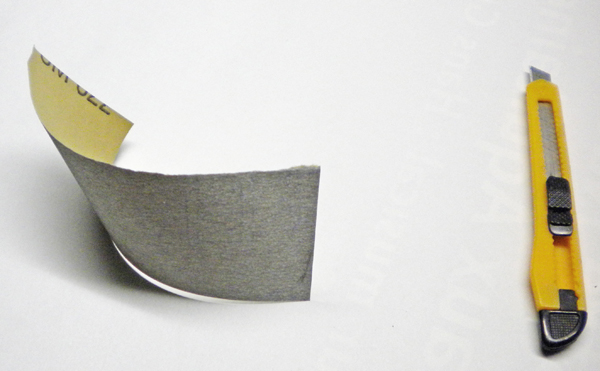 Papier de verre à grain fin recourbé posé à côté d'un cutter jaune