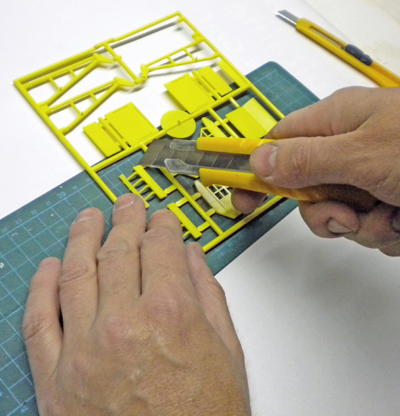 Mains détachant une pièce d'une grappe plastique jaune avec un cutter sur tapis de découpe