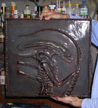 Maquettiste tenant un bas relief patiné représentant la créature Alien dans son atelier